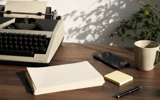 Typewriter beside a smartphone and cream paper stack in morning light