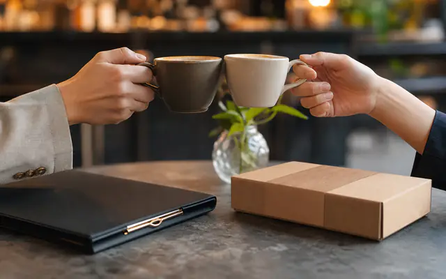Two coffee cups and a kraft-wrapped sample box on a cafe partnership table